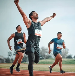 Runner crossing the finish line with arms raised in victory, leading the pack